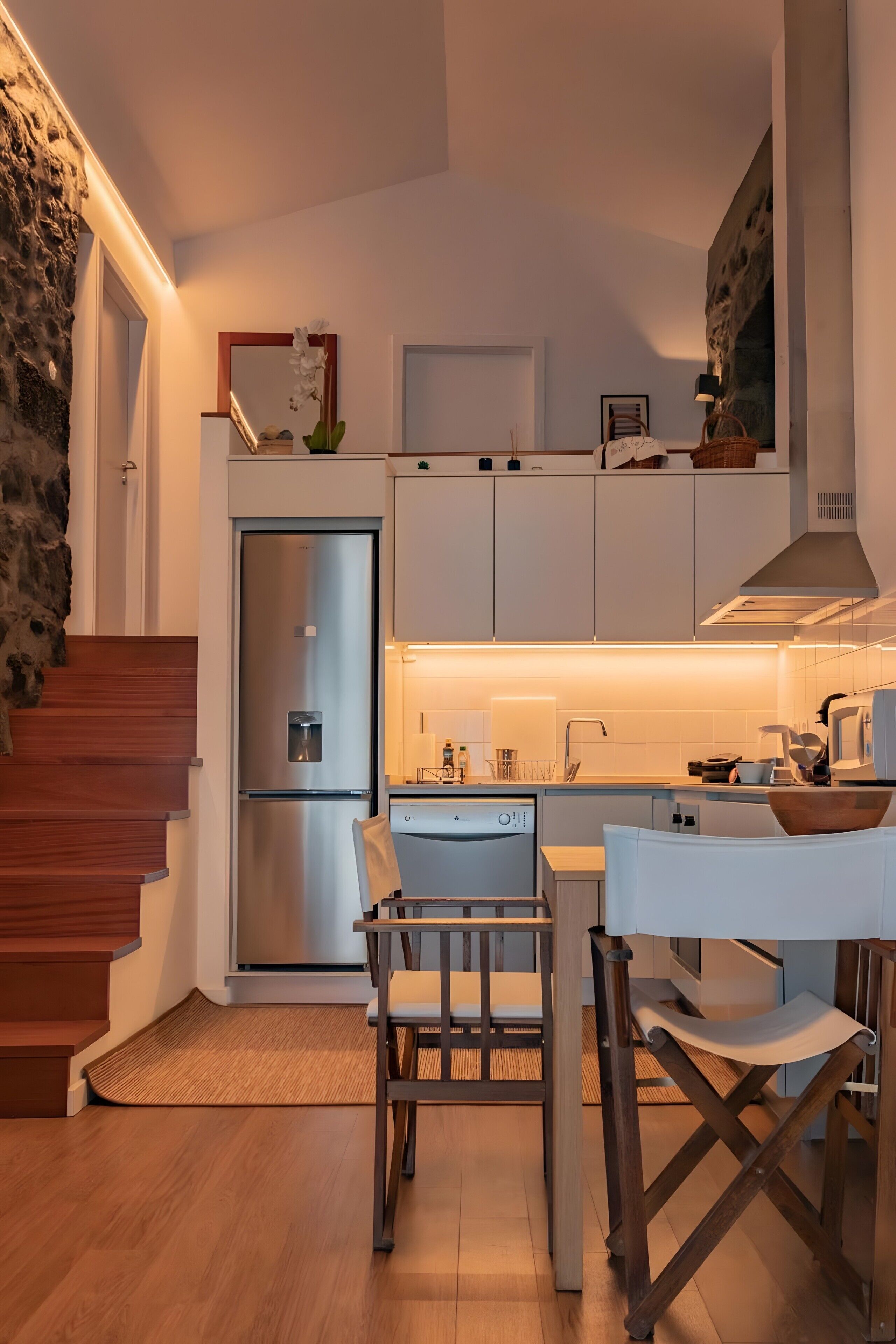 A modern kitchen with a built-in dishwasher, a stainless steel refrigerator, and a dining area with a wooden table and chairs.