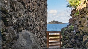 Eine Steinsmauer mit einem hölzernen Tor, das zu einem Gewässer und einer entfernten Insel führt.