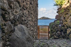 A stone wall with a wooden gate leading to a body of water and a distant island. - Holiday Home 'Casa de Pedra' with Sea View, Private Terrace and Wi-Fi (Praia)