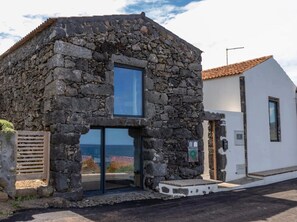 A stone building with a glass door and a view of the sea. - Holiday Home 'Casa de Pedra' with Sea View, Private Terrace and Wi-Fi (Praia)