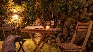 Ein Sitzbereich im Freien mit Tisch, Stühlen, einem Buch, einer Kerze und einer Weinflasche.
