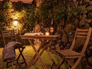 An outdoor seating area with a table, chairs, a book, a candle, and a bottle of wine. - Holiday Home 'Casa de Pedra' with Sea View, Private Terrace and Wi-Fi (Praia)