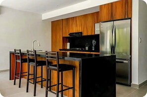 Une cuisine moderne dotée d’un îlot central, de tabourets de bar, d’un réfrigérateur en acier inoxydable et de meubles de rangement en bois.