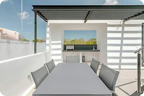 Une terrasse extérieure avec une table et des chaises, un barbecue et une vue sur la verdure.