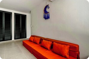 A room with a red sofa, a wall-mounted crescent moon decoration, and a sliding door with black blinds. - Modern Oasis Near the Beach (Q.R.)