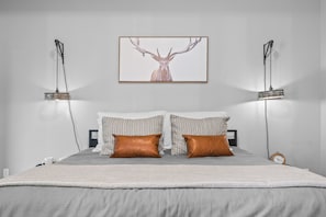 A bedroom with a bed, two bedside lamps, a clock, and a framed deer artwork on the wall.