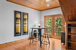 Une pièce avec un plafond en bois, une table avec deux chaises, une fenêtre donnant sur des arbres et une bibliothèque en bois.