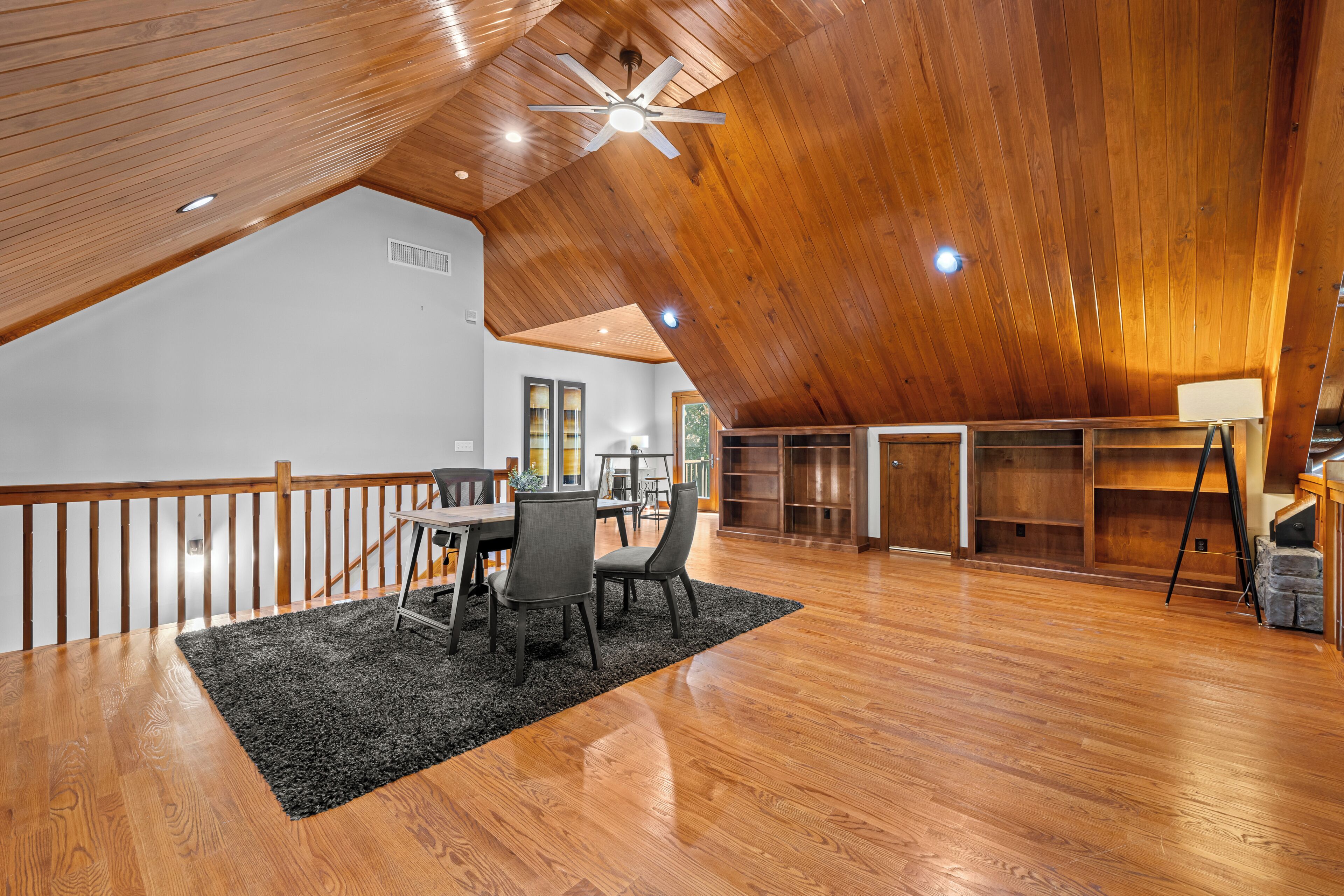 A spacious loft with a high ceiling, wooden beams, a dining area with a table and chairs, and a large window providing natural light.