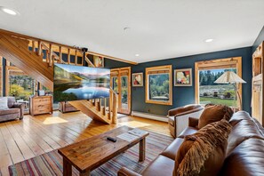 Un salon spacieux doté d’un grand téléviseur, de meubles en bois et de grandes fenêtres offrant une vue sur l’extérieur.