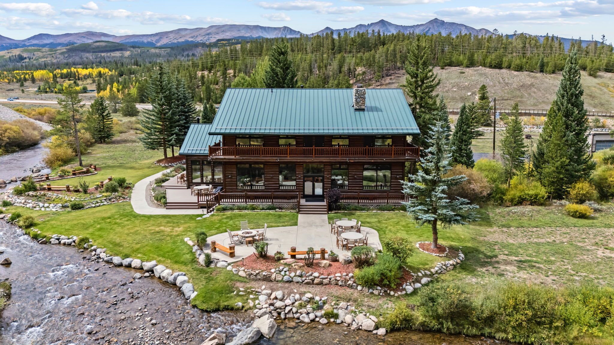 Una cabaña con techo verde, rodeada por un paisaje natural con un río y montañas al fondo.