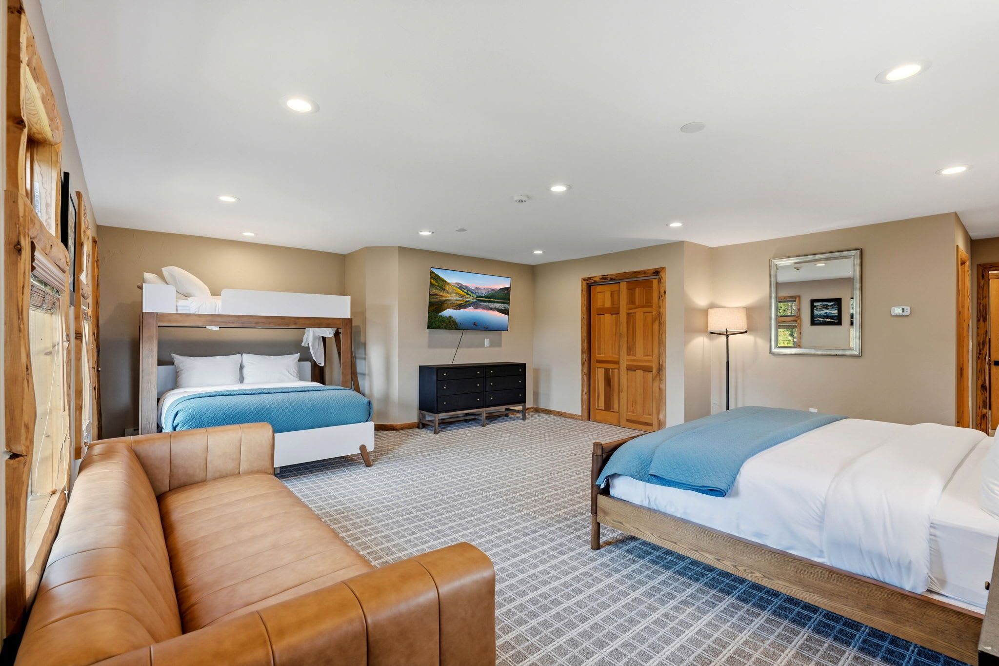 A hotel room with a bunk bed, a sofa, a flat-screen TV, a dresser, and a wooden door.
