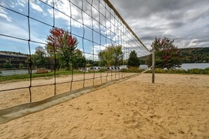 Une plage de sable avec un filet de volley-ball, des arbres et une étendue d’eau en arrière-plan.