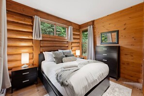 A wooden-paneled bedroom with a bed, bedside tables, and a dresser. - Rustic Retreat | 3BR Chalet | Fireplace | 8 guest (Lac-Supérieur)