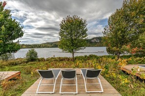 A wooden deck with three lounge chairs facing a lake. - Rustic Retreat | 3BR Chalet | Fireplace | 8 guest (Lac-Supérieur)
