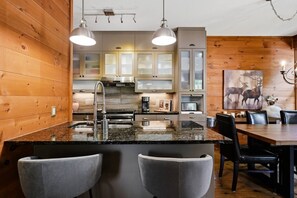 A modern kitchen with granite countertops, stainless steel appliances, and wooden paneling. - Rustic Retreat | 3BR Chalet | Fireplace | 8 guest (Lac-Supérieur)