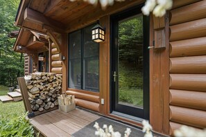A log cabin with a wooden deck, a stack of firewood, and a black door with a glass panel. - Rustic Retreat | 3BR Chalet | Fireplace | 8 guest (Lac-Supérieur)