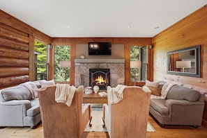 A log cabin interior with a fireplace, two sofas, and a television. - Rustic Retreat | 3BR Chalet | Fireplace | 8 guest (Lac-Supérieur)