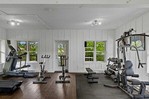 A gym with exercise equipment, wooden floors, and large windows. - Rustic Retreat | 3BR Chalet | Fireplace | 8 guest (Lac-Supérieur)