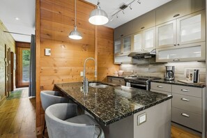 A modern kitchen with granite countertops, stainless steel appliances, and wooden paneling. - Rustic Retreat | 3BR Chalet | Fireplace | 8 guest (Lac-Supérieur)