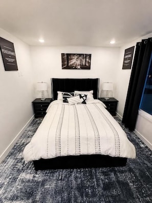Quarto com uma cama grande, duas mesas de cabeceira com luminárias, uma cabeceira e duas fotos emolduradas na parede.