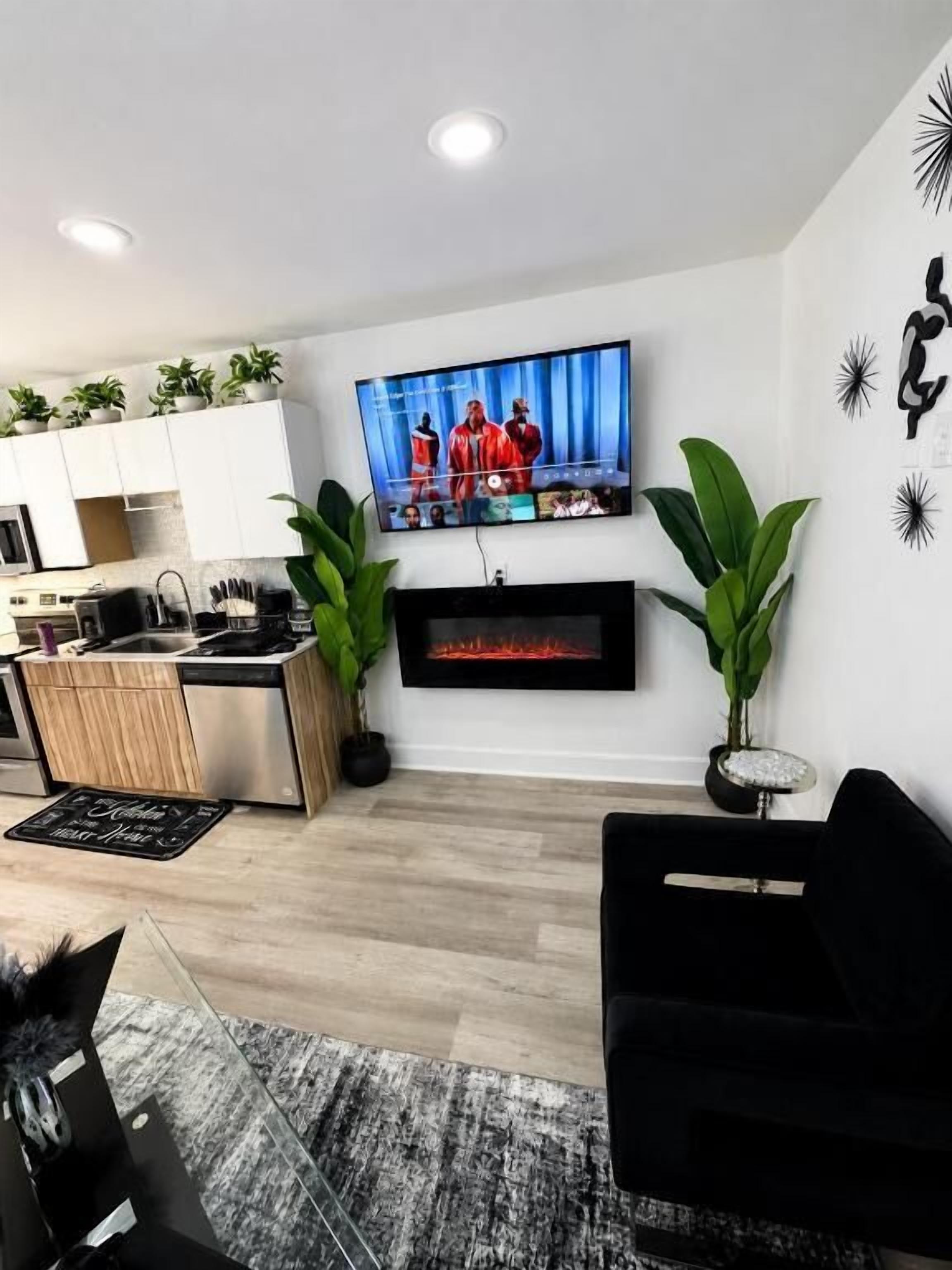 Ein modernes Wohnzimmer mit einem flachbildfernseher an der Wand, einem schwarzen Sofa und einem Kamin darunter.