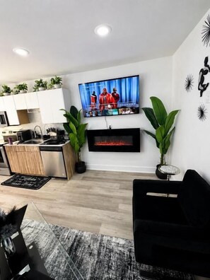 A modern living room with a flat-screen TV mounted on the wall, a black sofa, and a fireplace below. - Modern Oasis Near Deep Ellum (Dallas)