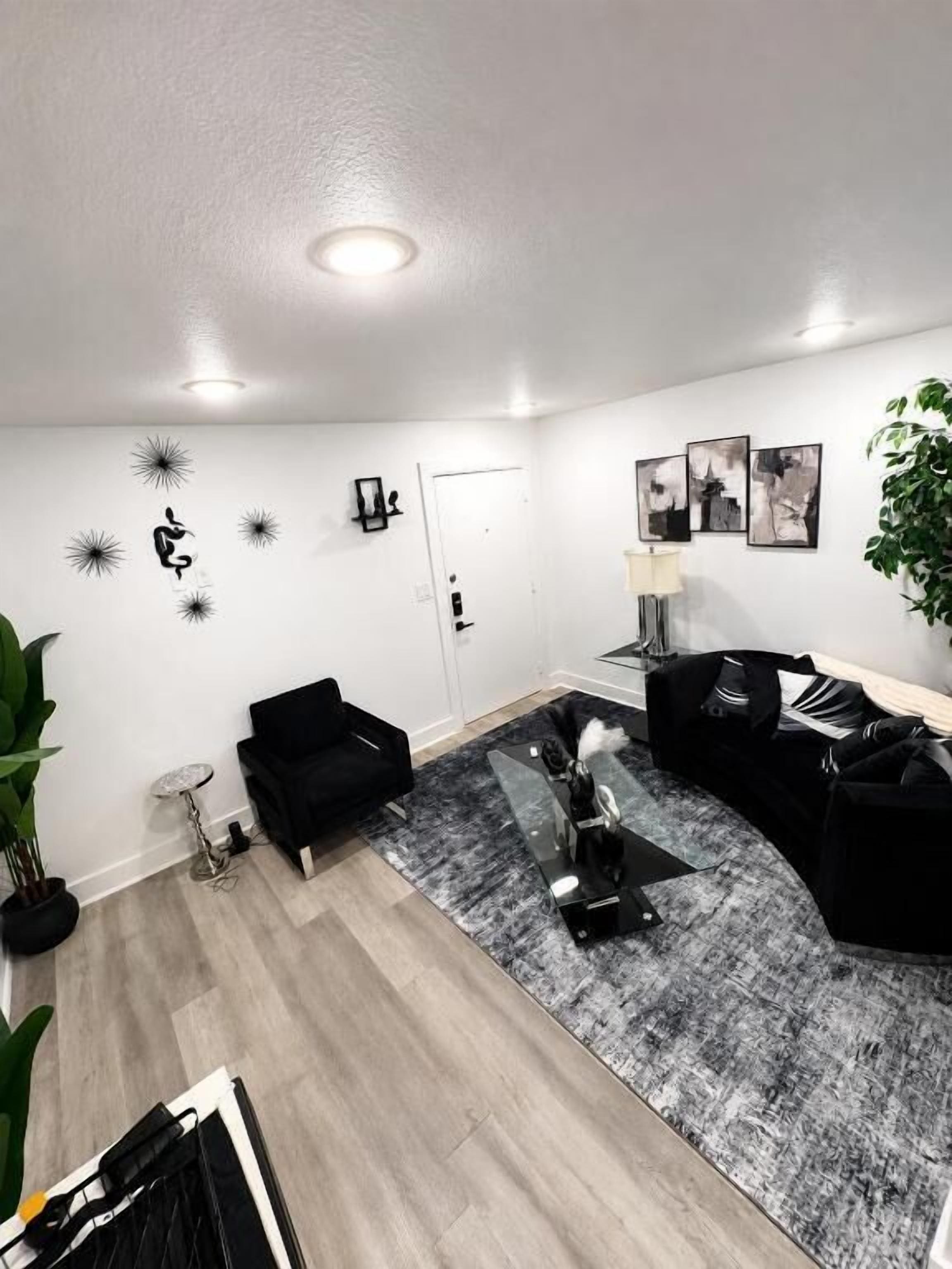 Una sala de estar moderna con un sofá negro, una mesa de centro de cristal y una alfombra gris estampada.