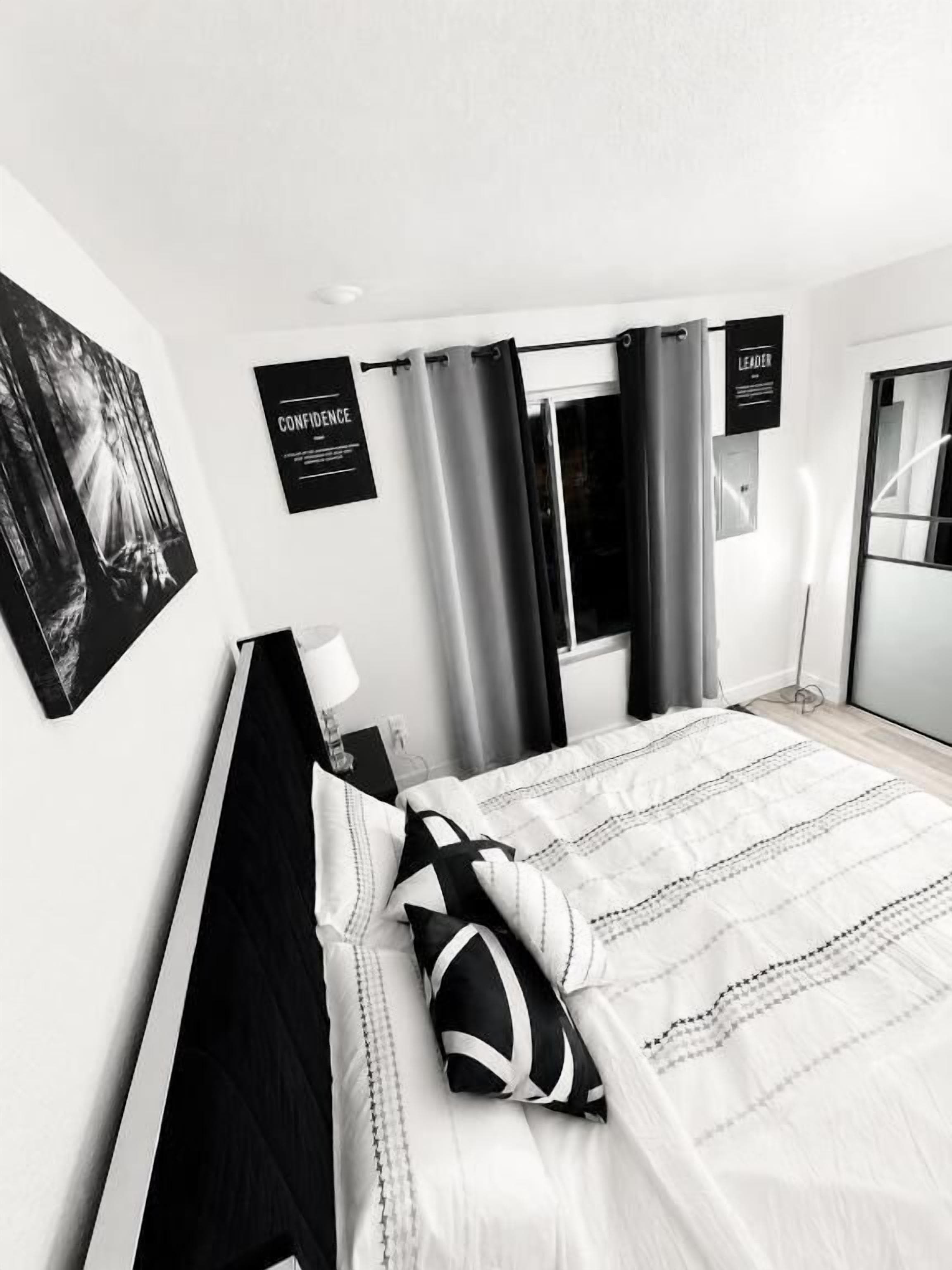 Ein modernes Schlafzimmer mit einem Bett, Vorhängen, einer Wandleuchte und einem Poster.