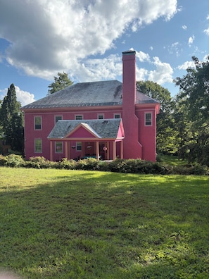 A large, pink house with a prominent chimney, surrounded by a well-maintained lawn and trees.