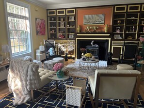 A cozy living room with a fireplace, comfortable seating, and a bookshelf filled with various items.