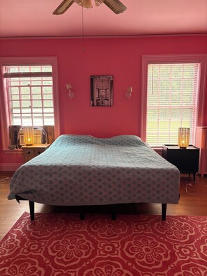 A bedroom with a bed, a window, a wall-mounted picture, and a ceiling fan.