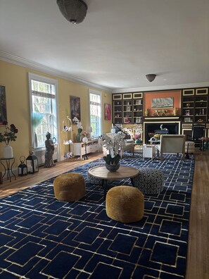 A spacious living room with a patterned rug, a fireplace, and a bookshelf.