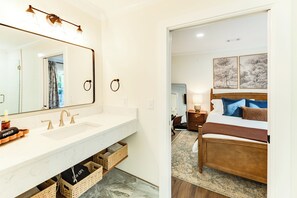 Un baño de hotel con un espejo grande, lavamanos dobles y un mueble de tocador con cestas de almacenamiento.