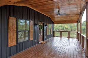 Un porche cubierto con piso de madera, ventilador de techo y ventanas grandes con contraventanas de madera.
