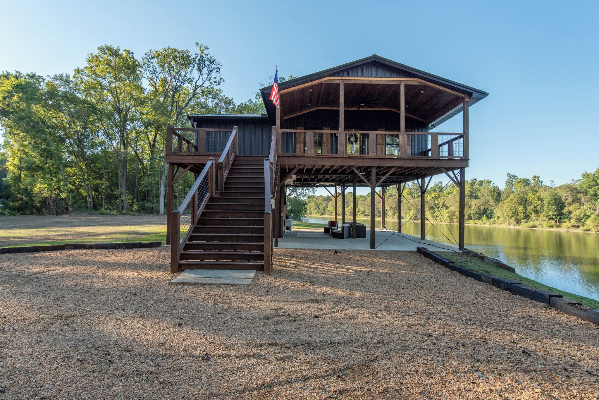 A two-story wooden cabin with a deck and stairs, overlooking a lake.
