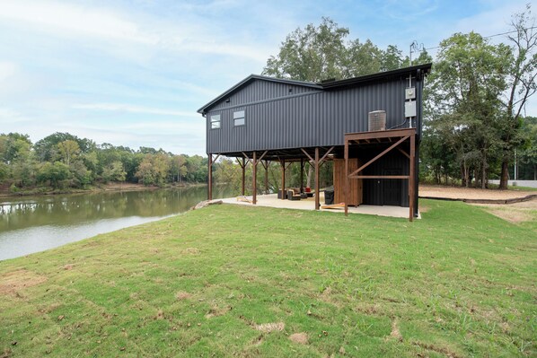 A modern outdoor deck with a metal structure, a grassy area, and a body of water in the background.