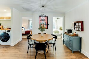 Una cocina moderna con comedor, lavadora y una habitación visible a través de una puerta abierta.