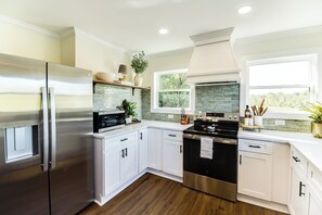Una cocina moderna con armarios blancos, electrodomésticos de acero inoxidable y vistas al exterior a través de una ventana.