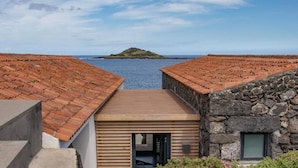 A coastal property with terracotta-tiled roofs, a stone building, and a view of a small island across the water.