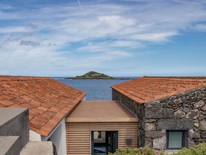 A coastal property with terracotta-tiled roofs, a stone building, and a view of a small island across the water.