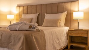 A neatly made bed with a headboard, two bedside lamps, and a wooden nightstand with a drawer.