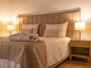 A neatly made bed with a headboard, two bedside lamps, and a wooden nightstand with a drawer.