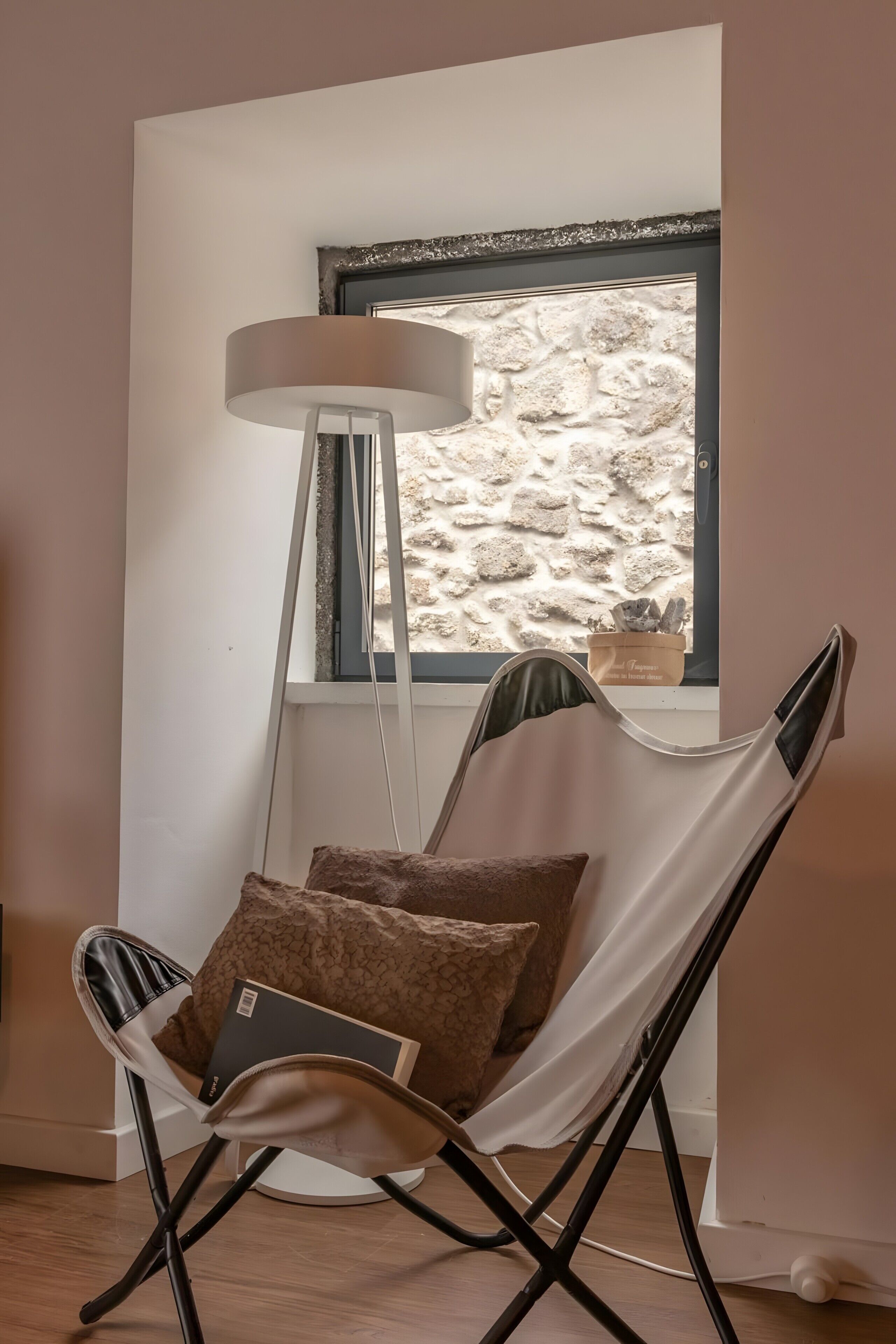 Ein Zimmer mit Fenster, einer Stehlampe und einem Sessel mit Kissen.