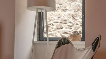 Ein Zimmer mit Fenster, einer Stehlampe und einem Sessel mit Kissen.