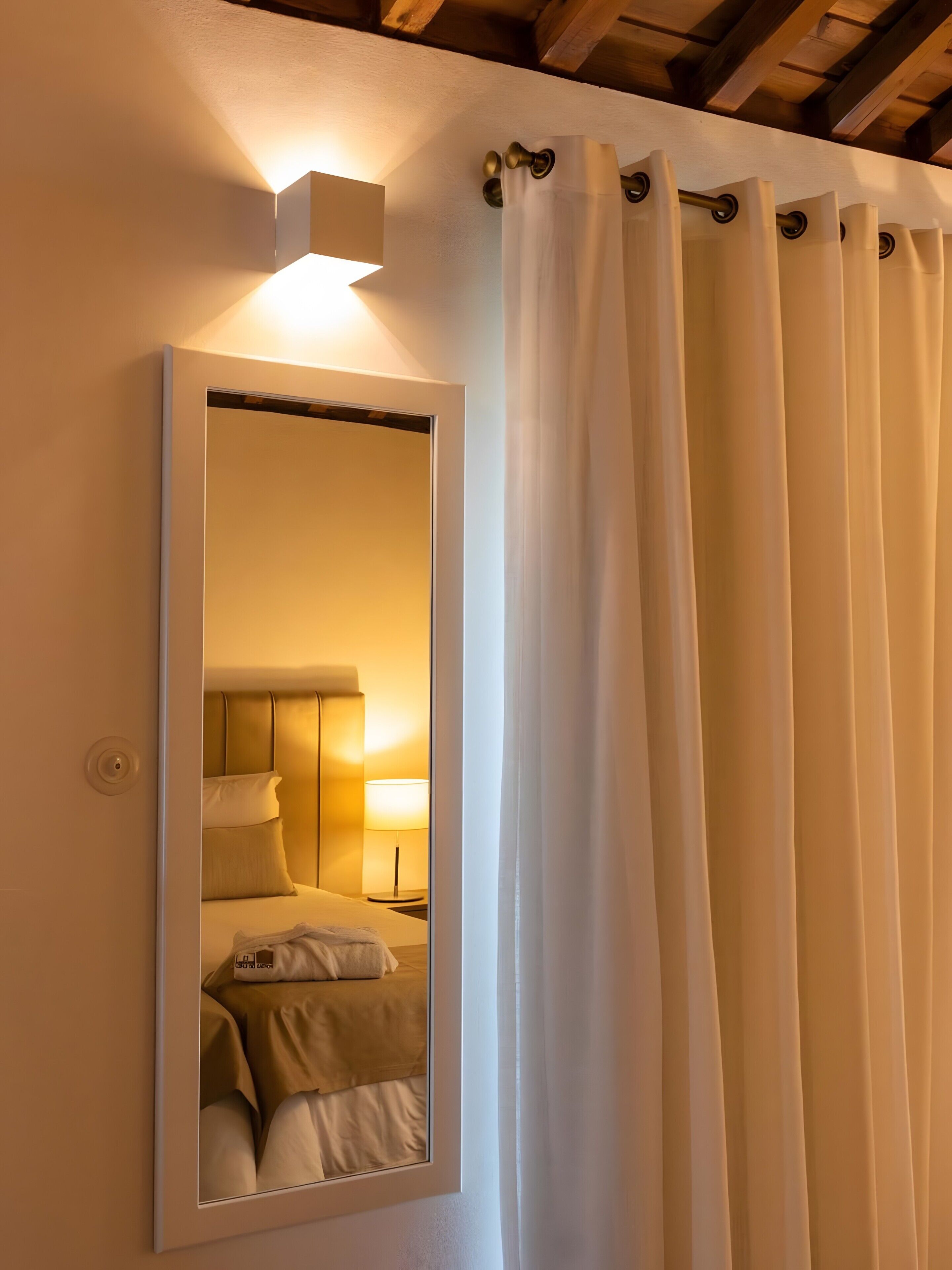 Ein Spiegel zeigt das Schlafzimmer mit einem Bett, einem Nachttisch und einer Lampe.