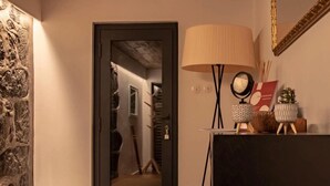 A room with a door leading to a staircase, a lamp, a mirror, and a small table with decorative items.