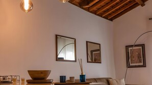 A room with a wooden ceiling, a sofa, a table with a bowl and cups, and framed pictures on the wall.
