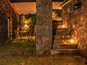 A stone staircase leading to a covered outdoor area with a table and chairs, and two lantern-style lights.