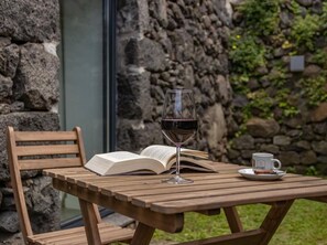 A wooden table with a glass of red wine, an open book, and a cup with a saucer.