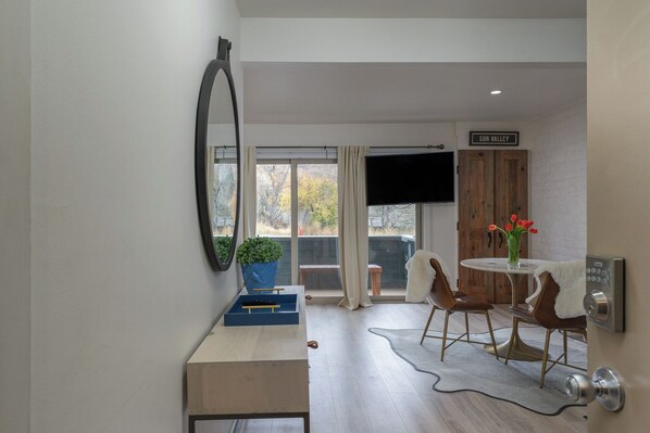 Une chambre moderne avec un bureau en bois, une table ronde avec des chaises, un téléviseur et un panneau indiquant « SUN VALLEY ».